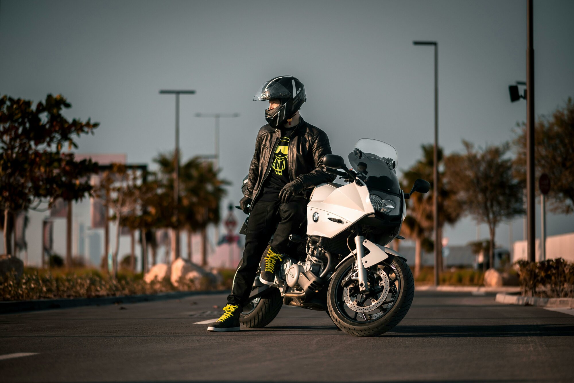 Muž stoj&iacute; pri motorke bielej farbe a na hlave m&aacute; čiernu prilbu pre motork&aacute;ra.