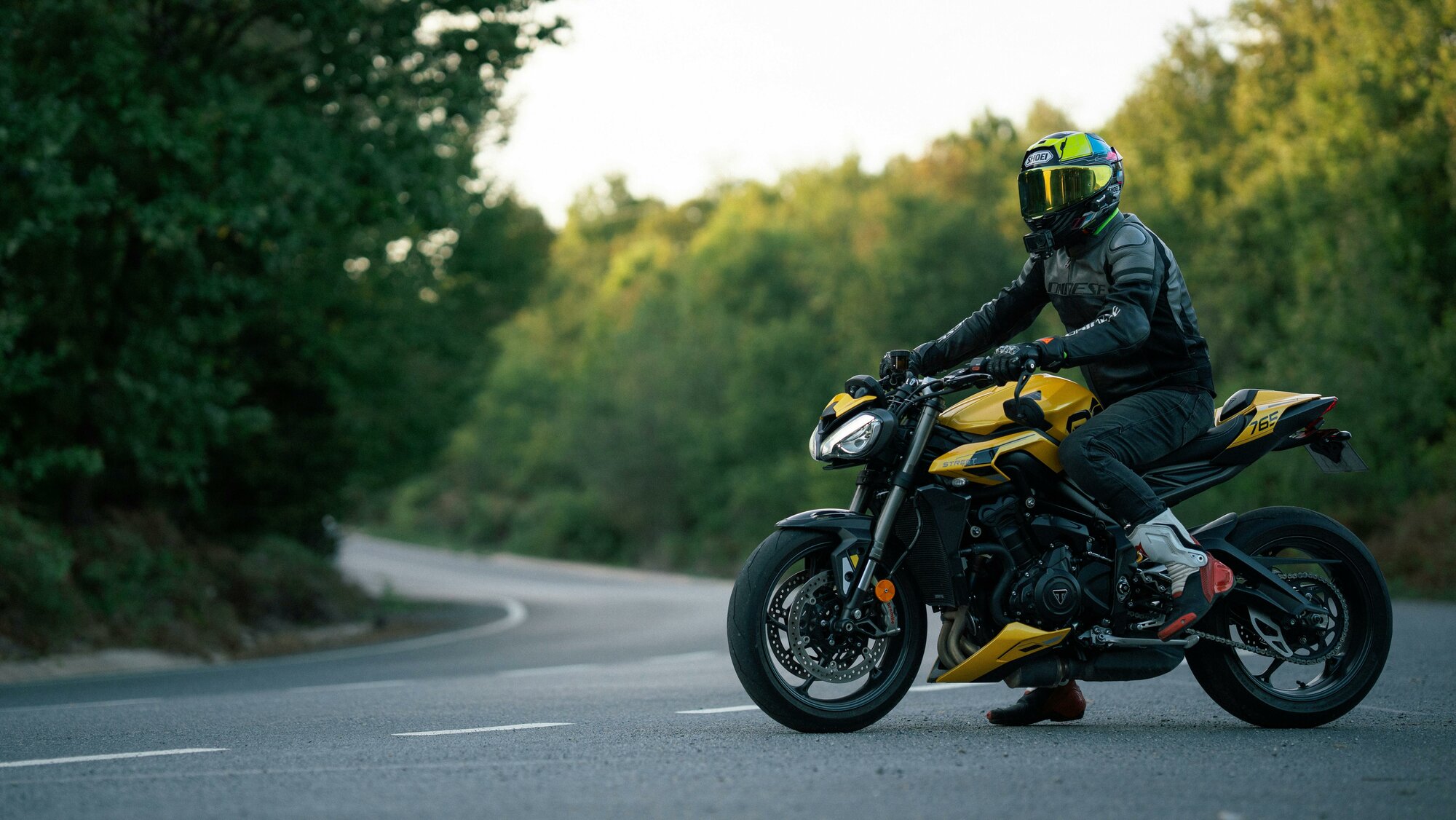 Motorkár sedí na žlto-čiernej motorke na ceste v prilbe a nepremokavom motorkárskom oblečení